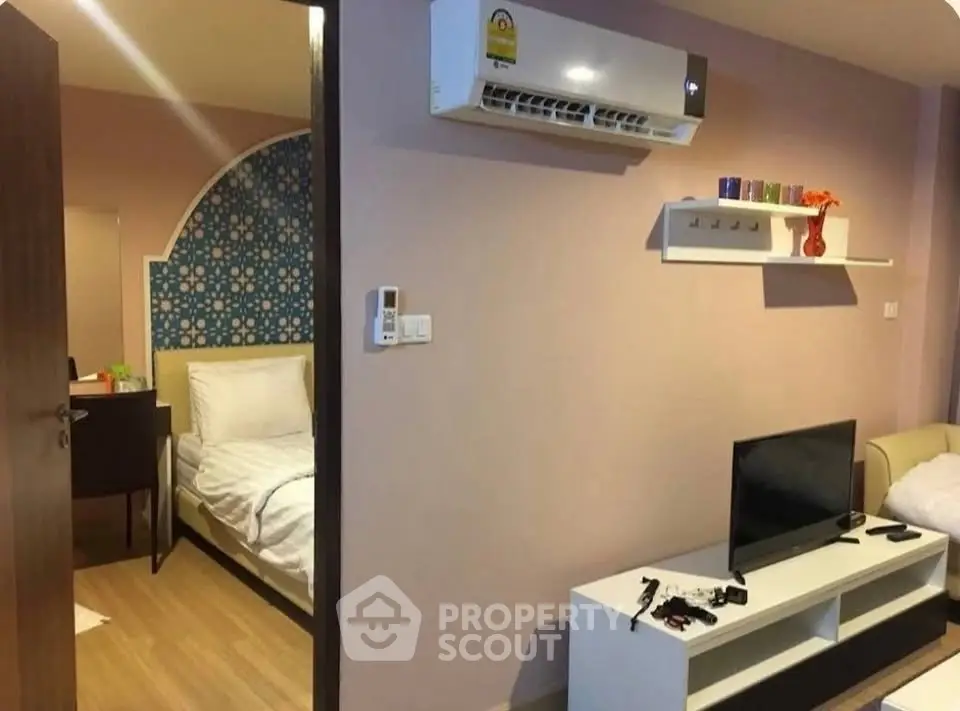 Cozy living room with modern decor and adjacent bedroom, featuring air conditioning and stylish shelving.