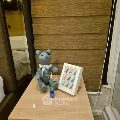 Cozy bedroom corner with plush teddy bear and framed art on wooden nightstand.