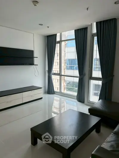 Spacious living room with large windows and modern furniture in a high-rise apartment.