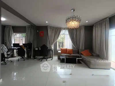 Spacious living room with modern decor and elegant chandelier, featuring a cozy sectional sofa and large windows.