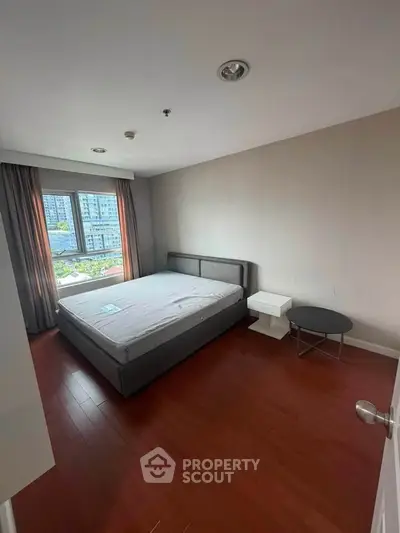 Spacious bedroom with large window and modern furnishings in a high-rise apartment.