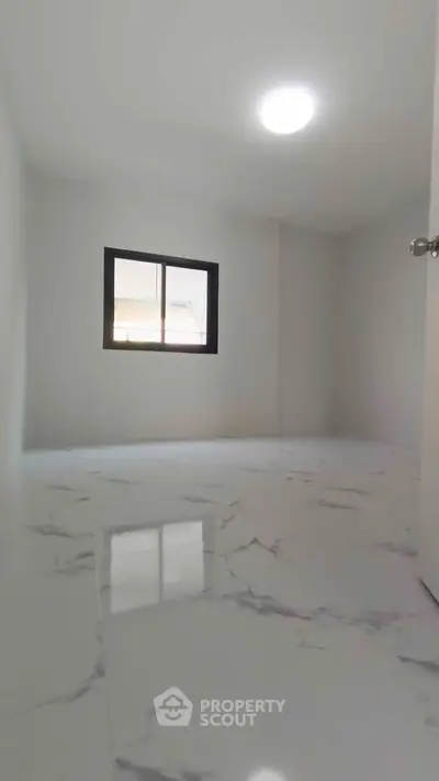 Spacious empty room with marble flooring and a window, ideal for customization.