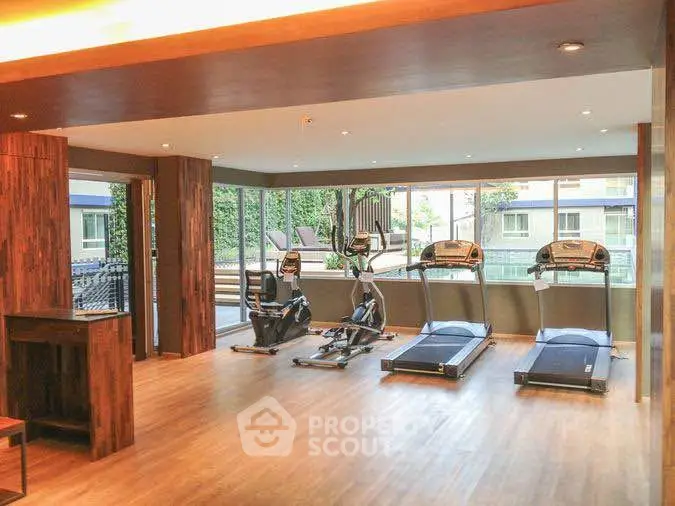Spacious gym with modern equipment and large windows in luxury apartment complex.