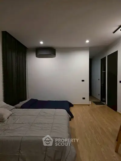 Modern bedroom with minimalist design and cozy ambiance, featuring a comfortable bed and sleek wooden flooring.