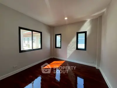 Spacious sunlit room with polished wooden floors and large windows in modern home.