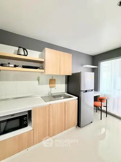 Modern kitchen with sleek cabinets, stainless steel fridge, and microwave in a bright apartment.