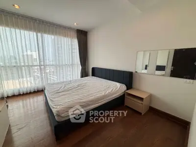 Spacious bedroom with large window offering city views, featuring a modern bed and wooden flooring.