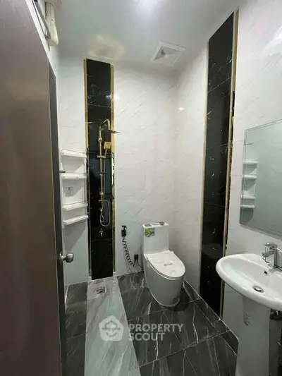 Modern bathroom with sleek black and white tiles, featuring a shower, toilet, and sink.