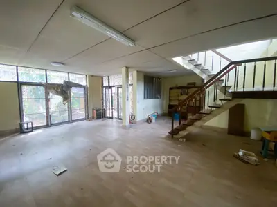 Spacious living room with large windows and staircase, ideal for renovation.