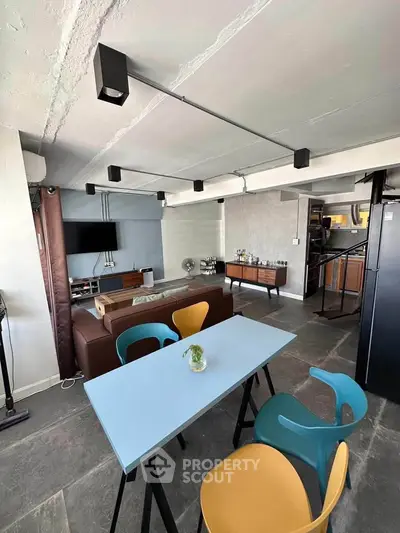 Modern industrial-style living room with open layout and colorful chairs, featuring sleek furniture and exposed ceiling.