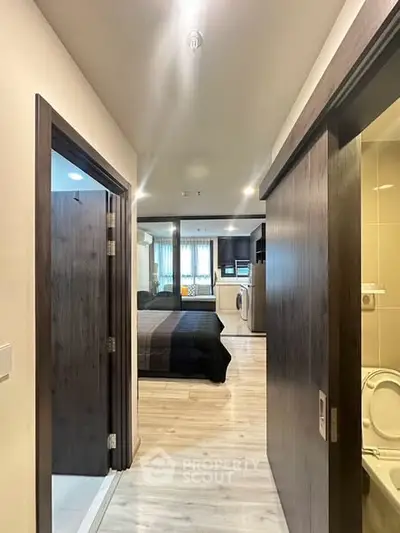 Modern apartment hallway leading to a cozy bedroom with stylish decor and a glimpse of a compact kitchen.