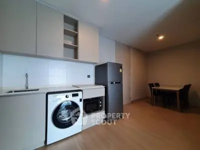 Modern kitchen with washing machine, fridge, and dining area in open layout.