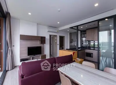 Modern open-layout living room with kitchen, featuring sleek furniture and large windows for natural light.