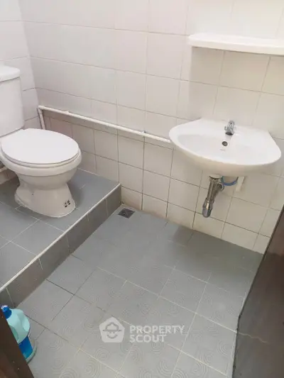 Compact bathroom with white tiles, toilet, and sink, ideal for small spaces.