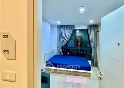 Modern bedroom with large window and blue bedding in a high-rise apartment.