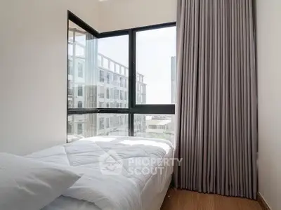 Cozy bedroom with large window offering city view, featuring modern decor and ample natural light.