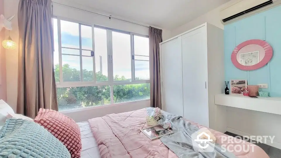 Charming bedroom with large window and pastel decor, offering serene garden views.