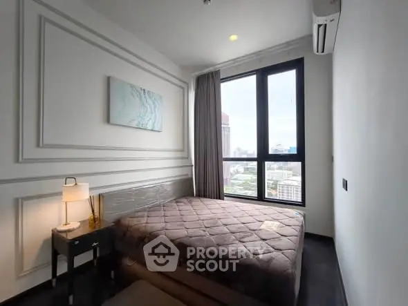 Modern bedroom with large window offering city view, featuring elegant decor and cozy ambiance.
