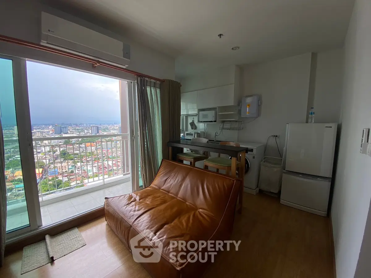 Modern studio apartment with leather sofa and city view balcony, featuring compact kitchen and large windows.