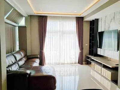 Spacious modern living room with leather sofa and large TV, featuring elegant curtains and sleek design.