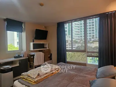 Cozy bedroom with large windows and urban view, featuring modern decor and ample natural light.