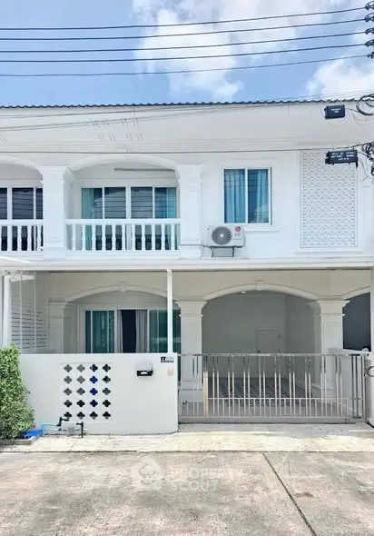 Charming two-story white townhouse with balcony and gated entrance, perfect for modern living.