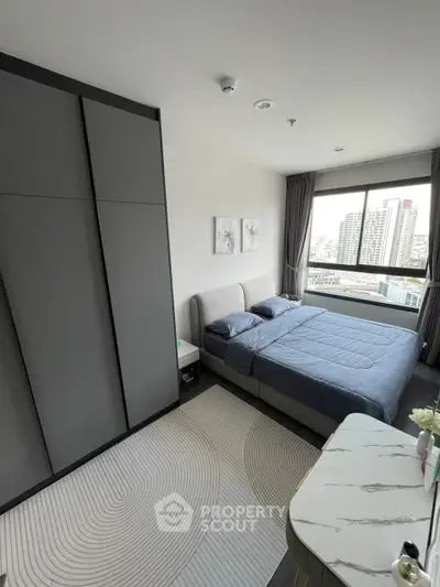 Modern bedroom with large window offering city view, sleek wardrobe, and stylish decor.
