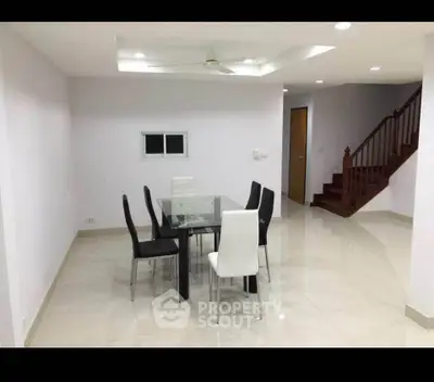 Spacious dining area with modern glass table and elegant chairs, featuring a sleek staircase and bright lighting.