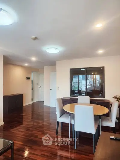 Spacious living room with elegant dining area and polished wooden floors in modern apartment.