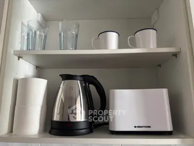 Modern kitchen shelf with kettle, toaster, mugs, and glasses for a cozy home setup.