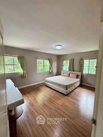Spacious bedroom with large windows and wooden flooring, offering a serene and bright atmosphere.