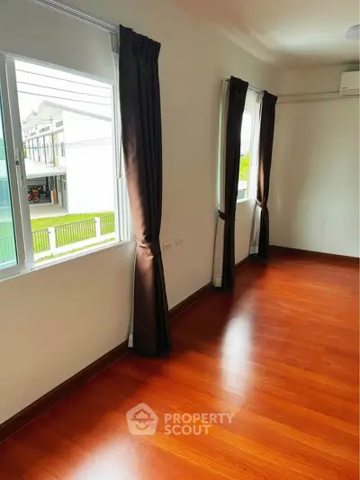 Spacious room with wooden flooring and large windows offering natural light.