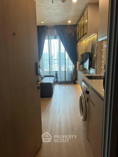 Modern apartment interior with open kitchen and living area, featuring a washing machine and city view.