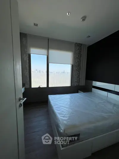 Modern bedroom with large window offering stunning city skyline view, featuring sleek design and ample natural light.