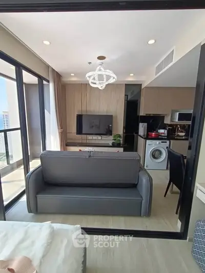 Modern living room with open kitchen and washing machine, featuring a sleek sofa and large windows with city view.