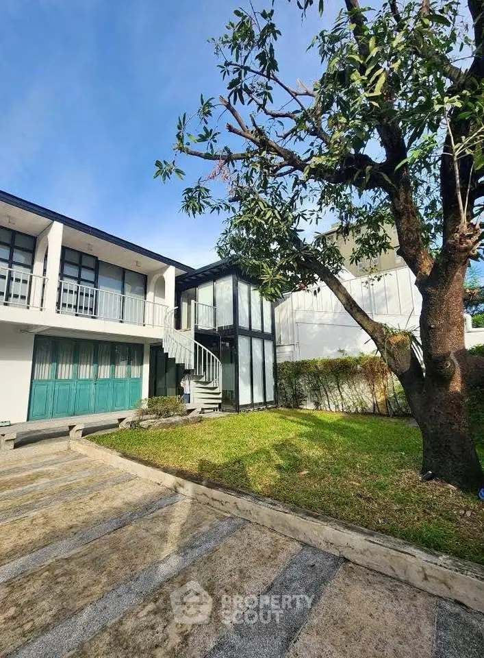 Modern two-story building with lush garden and tree, featuring a sleek exterior staircase.