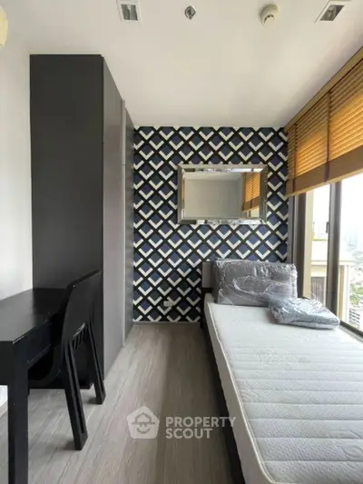 Modern bedroom with stylish wallpaper and city view, featuring a single bed and sleek black furniture.