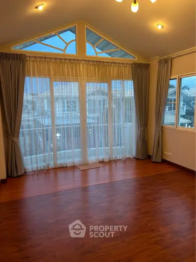 Spacious room with large windows and elegant curtains, featuring wooden flooring and a vaulted ceiling.