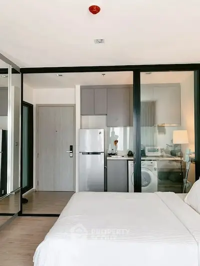 Modern studio apartment with glass partition, compact kitchen, and cozy bedroom.