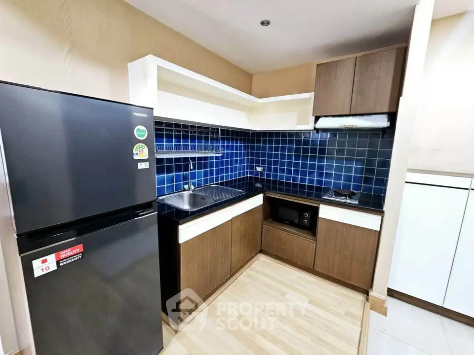 Modern kitchen with sleek cabinets, blue tile backsplash, and stainless steel appliances in a cozy apartment.
