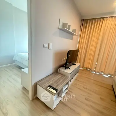 Modern living room with TV and wooden flooring adjacent to a cozy bedroom.