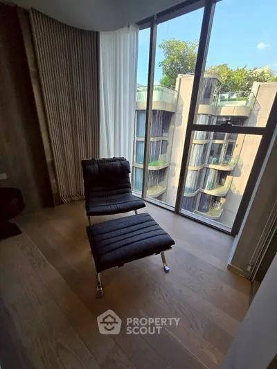 Modern apartment with stylish chair and floor-to-ceiling windows offering a stunning city view.