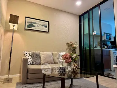 Modern living room with cozy sofa, glass coffee table, and sliding doors to kitchen
