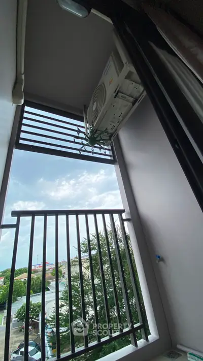 Modern balcony with air conditioning unit and scenic view of trees and sky.