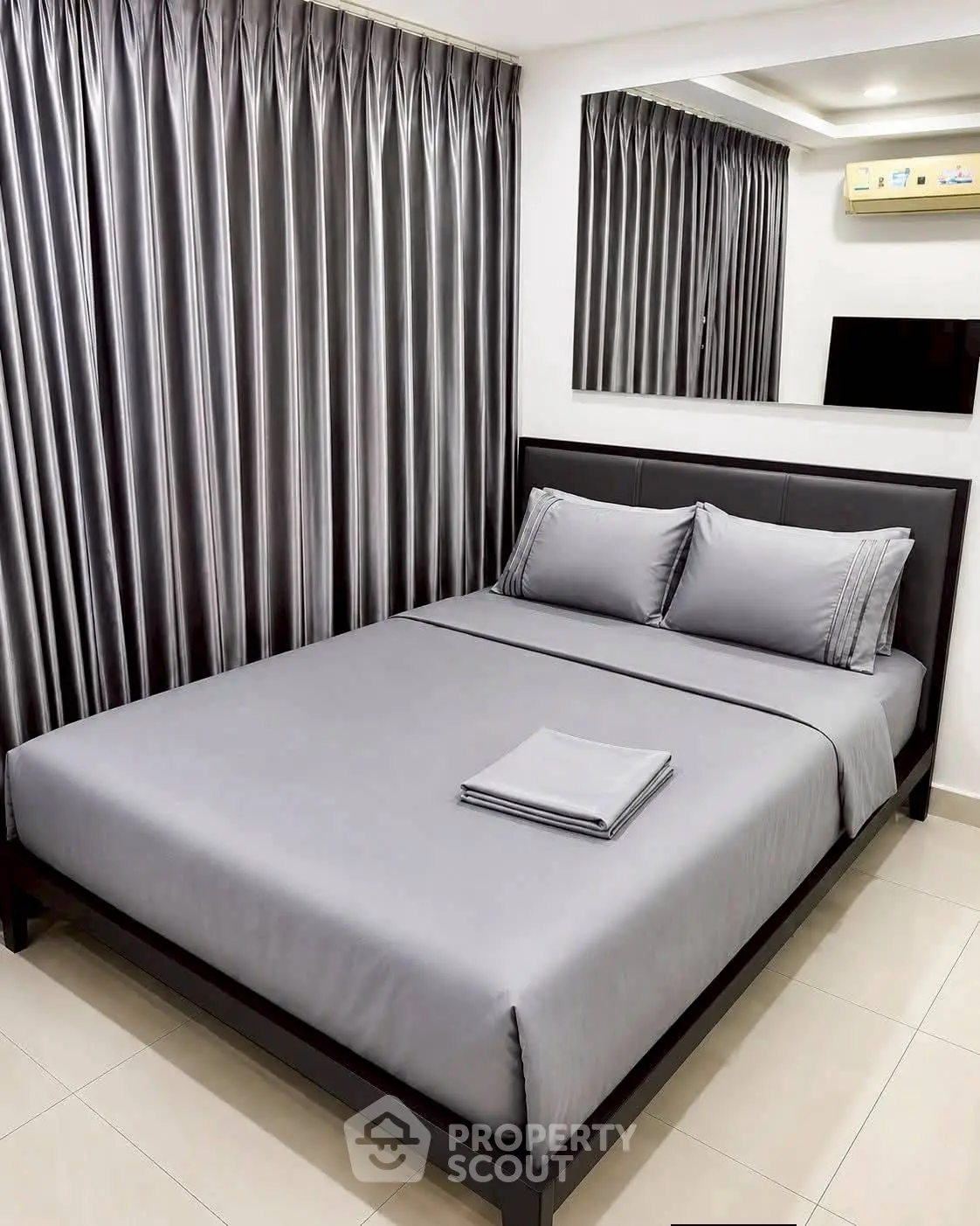 Modern bedroom with sleek gray bedding and stylish curtains, featuring a wall-mounted TV and air conditioning.