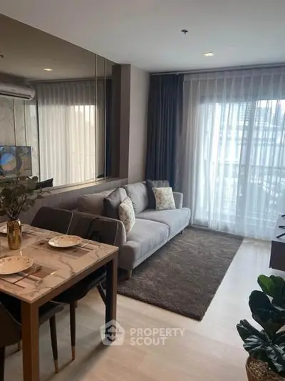 Modern living room with cozy sofa and dining area, featuring large windows and elegant decor.