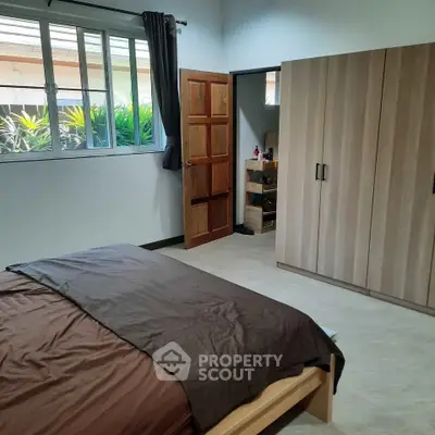 Spacious bedroom with large window and wooden wardrobe, offering a cozy and inviting atmosphere.