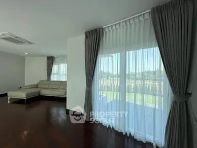 Spacious living room with elegant curtains and a cozy sofa, offering a serene view of the outdoors.
