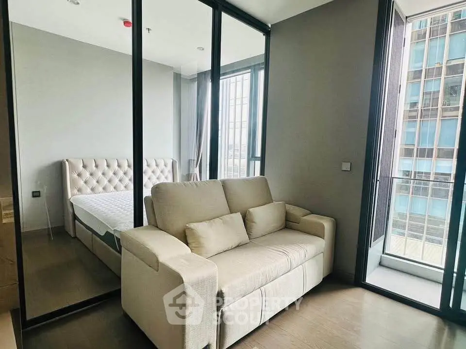 Modern bedroom with glass wall and cozy sofa, featuring a city view.
