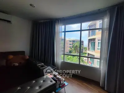 Cozy living room with large window offering a scenic view of lush greenery and modern buildings.